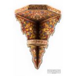 A Persian polychrome painted corner wall shelf, red ground with foliate motifs, 43cms