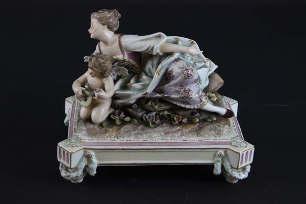 A Continental porcelain figure group of a young lady reclining with musical putto on plinth base