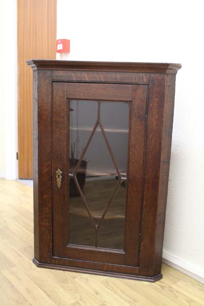 An early 20th Century oak hanging corner cupboard with astral glazed door opening onto 3 fixed