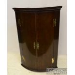 A late George III mahogany bow fronted hanging corner cupboard, the two doors opening to reveal four