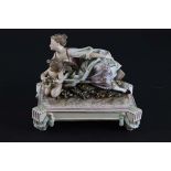 A Continental porcelain figure group of a young lady reclining with musical putto on plinth base