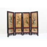 A Chinese black lacquer four fold table screen, enclosing four gold ground panels set with stained