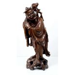 A Chinese carved wood figure of a standing man with sword to one side carrying loosely tied