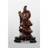 A Chinese carved wood figure of an Immortal standing holding a long scroll bag with crane to one