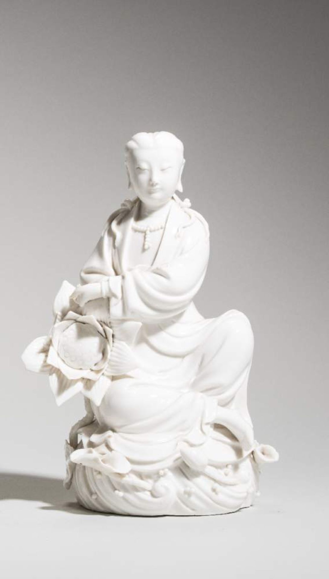 SITZENDE GUANYIN AUF WOGEBlanc de Chine. China, 20. Jh.Sitzende Göttin Guanyin auf einer Woge, mit