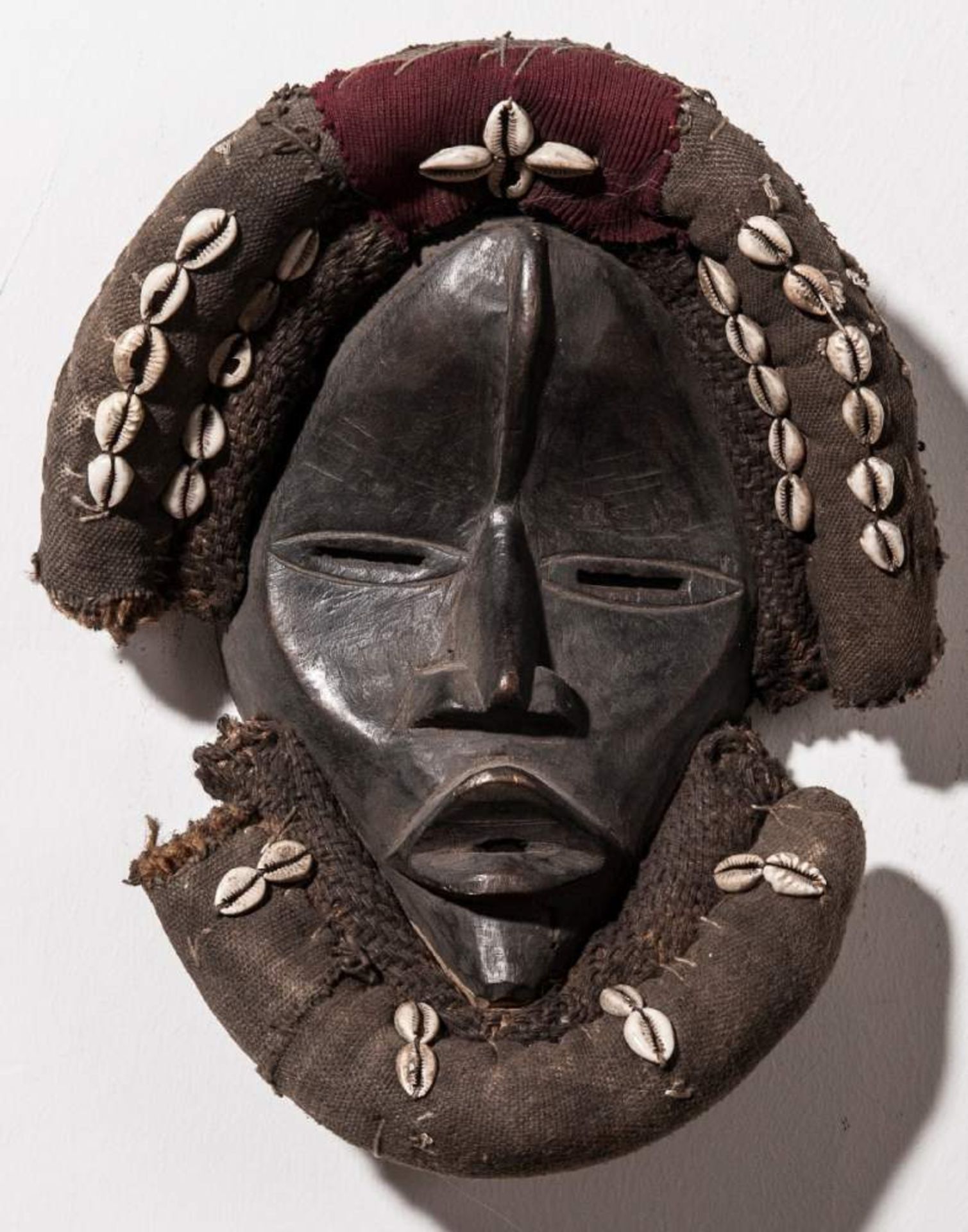 HOLZMASKE MIT KAURIMUSCHELN DER DANHolz, Muscheln, Stoff. Afrika, Liberia, 20. Jh.HÖHE 32 CM, BREITE