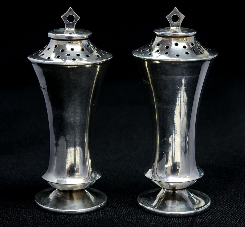 A pair of Edwardian silver pepperettes, of waisted conical form, with angular terminals,