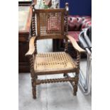 An early 20th Century oak Carolean style open armchair, with a canework back and seat,