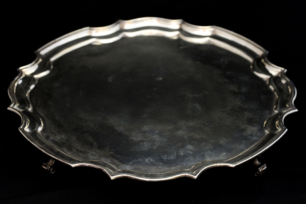 A George V silver salver, with Chippendale style border, atop four scroll form supports,