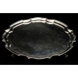 A George V silver salver, with Chippendale style border, atop four scroll form supports,