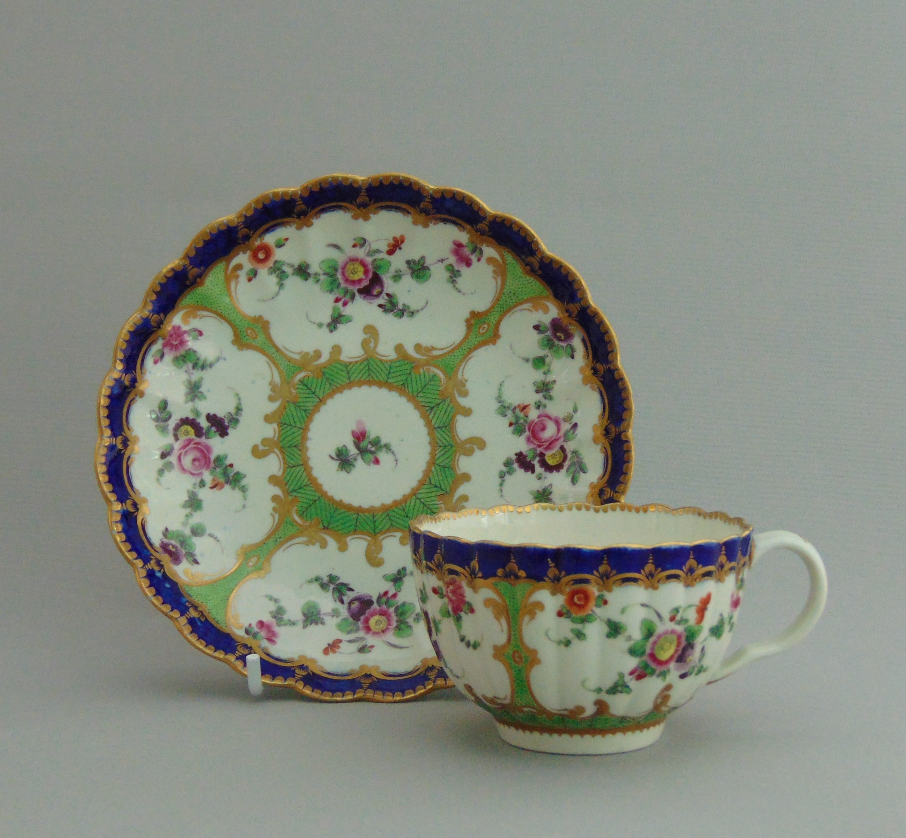 A Worcester tea cup and saucer, decorated with flowers within a green and blue border, circa 1775,