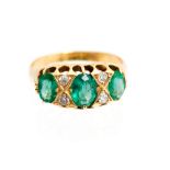 An emerald three stone boathead yellow gold ring, with diamond points between centre emerald,