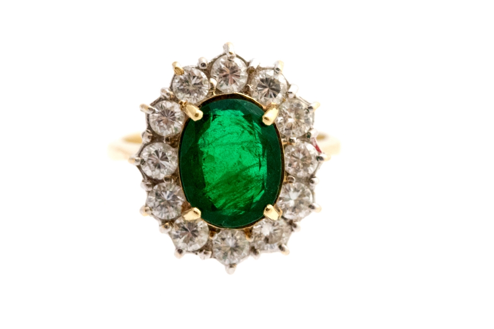 An emerald and diamond cluster ring, the centre oval emerald approx 10 x 7.