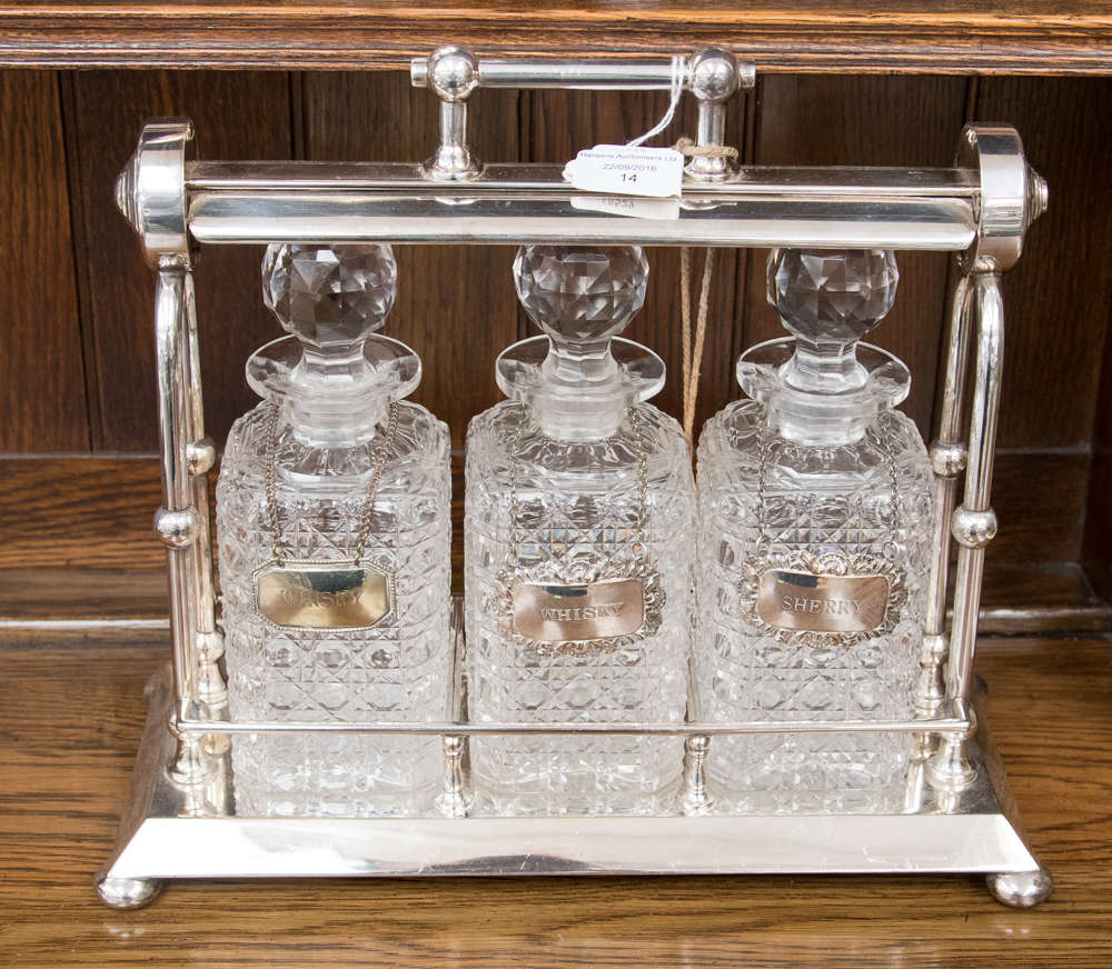 An early 20th Century silver plated tantalus containing three cut glass decanters and spirit labels,