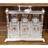 An early 20th Century silver plated tantalus containing three cut glass decanters and spirit labels,