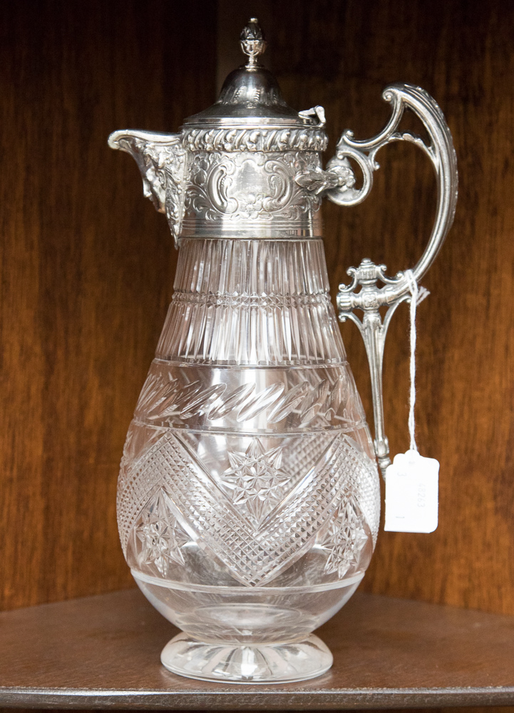 An electroplate mounted cut glass claret jug of baluster form with scroll handle, mask spout,