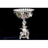 A Continental figural comport with applied roses to the basket bowl, below,