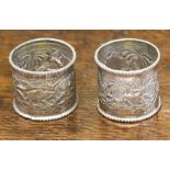 A pair of white metal cylindrical napkin rings, beaded rims, repousse decorated with elephants,