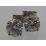 A pair of white metal and solitaire diamond stud earrings, set round cut stones of approx. 1.20