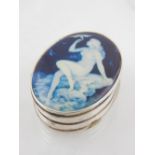 A white metal pill box of oval form, the hinged lid having blue and white enamel plaque depicting