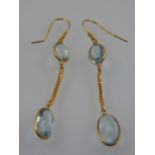 A pair of yellow metal and aquamarine double drop earrings, each set two oval cut stones.