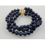 A black pearl triple strand bracelet, having yellow metal clasp.