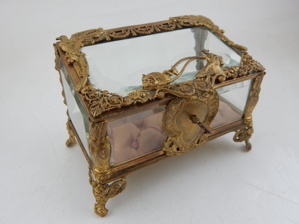 An early 20th century French gilt metal glass casket, the hinged slant front embossed with a dolphin