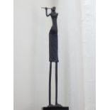 An African style cast iron figure of a woman playing the flute, raised on stepped base. H. 120cm