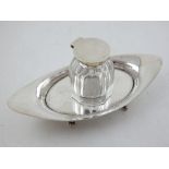 A George V silver inkstand, the detachable cut glass inkwell on elliptical stand with scroll feet,