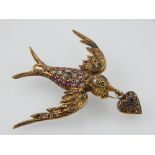 An early 20th century gem-set brooch in the form of a bird, wings outstretched and holding a heart