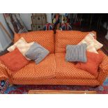 A modern designer two seater settee upholstered in patterned pale red fabric on mahogany feet with