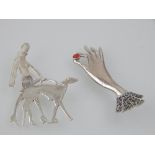 A white metal brooch, in the form of a lady walking her dog,