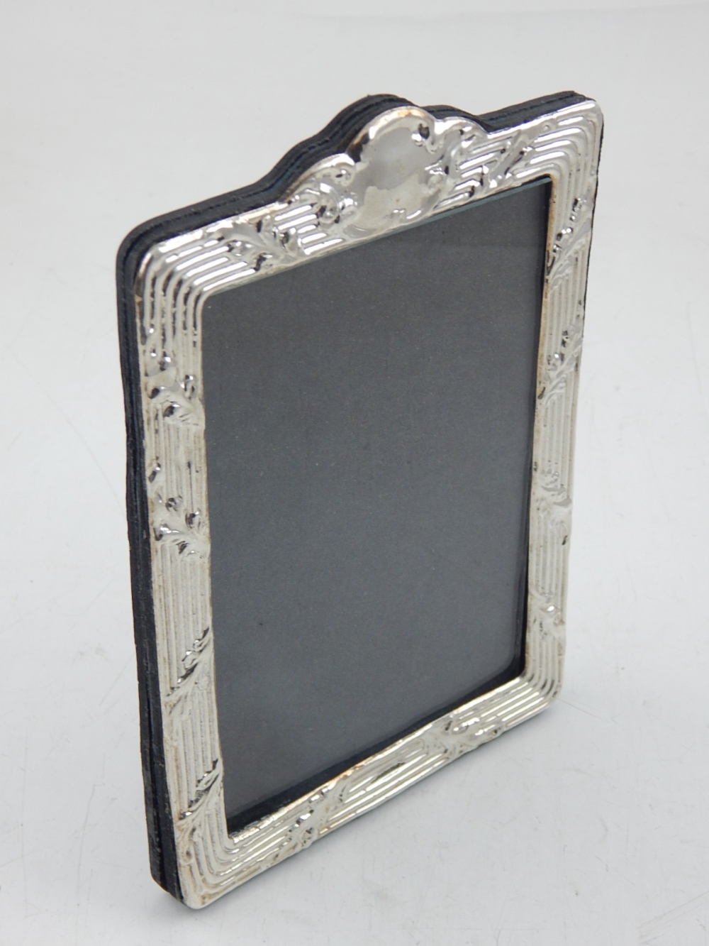 A silver easel back picture frame, with repousse leaf and thread border. H.