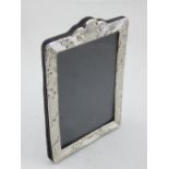 A silver easel back picture frame, with repousse leaf and thread border. H.