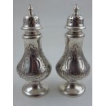 A pair of Victorian style silver baluster peppers, with embossed floral decoration around vacant