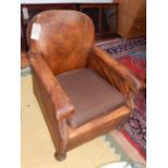 A vintage dark tan leather club armchair, with a brown fabric upholstered loose cushion, raised on