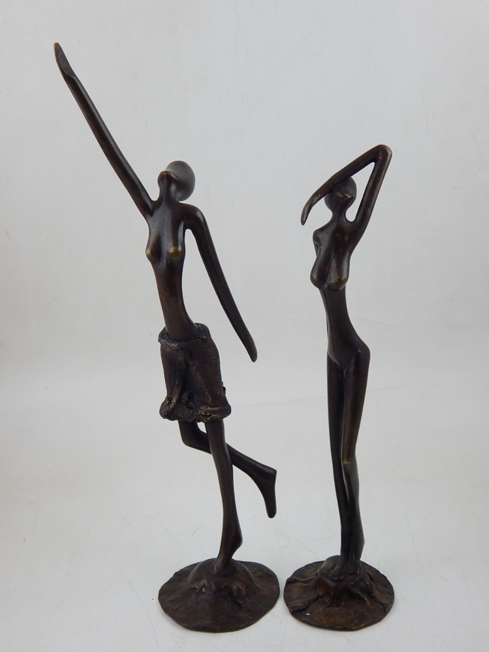 In the style of Giacometti, two female bronze studies on circular bases, tallest H.