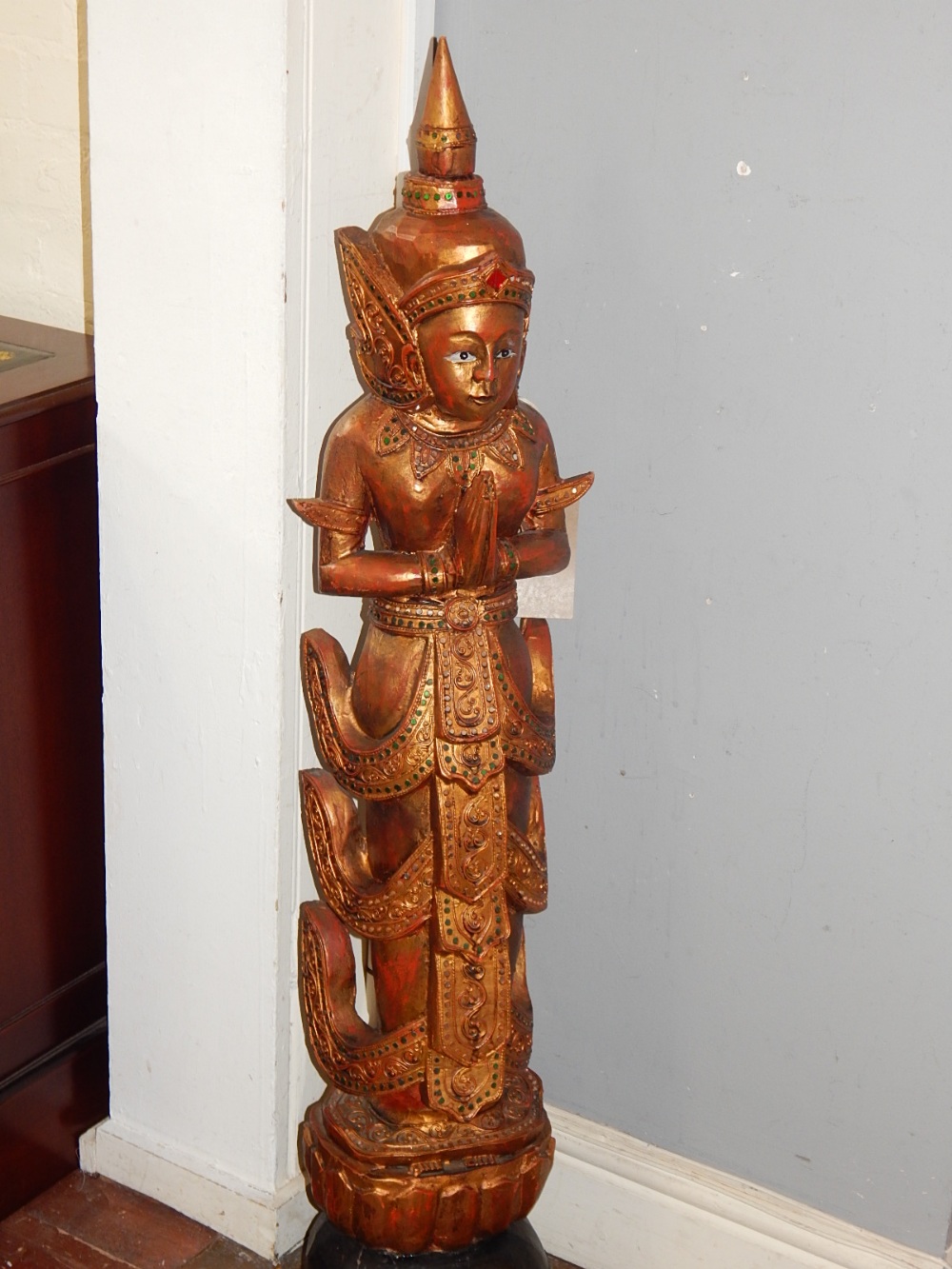 An Indo-China carved wooden deity at prayer standing on a lotus blossom,