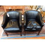 A pair of black leather tub shaped chairs, with loose cushions and raised on square tapering legs,