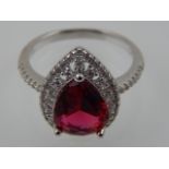 A silver and cubic zirconia dress ring, claw set central red pear shaped stone.