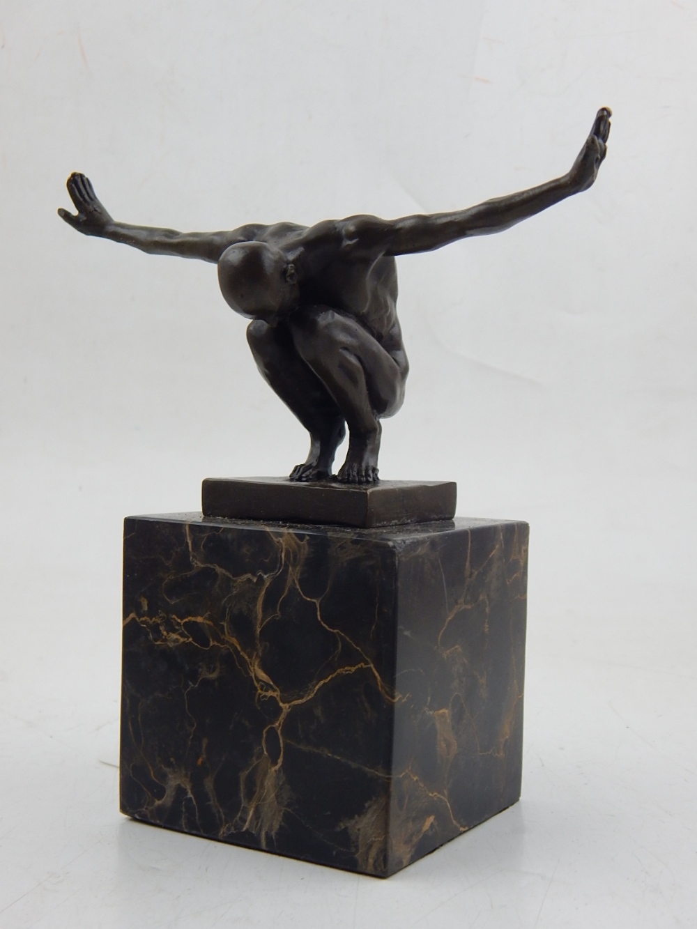 A contemporary bronze of a nude crouching man, arms outstretched and palms outwards,