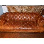 A Chesterfield cognac leather three seater sofa, button back upholstered, raised on squat ball feet.