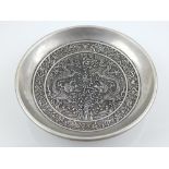 A Chinese white metal dish, the interior decorated with dragons chasing a flaming pearl within a