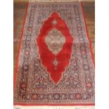 A red ground Keshan rug, decorated with teardrop medallion to centre, within floral borders, 155cm