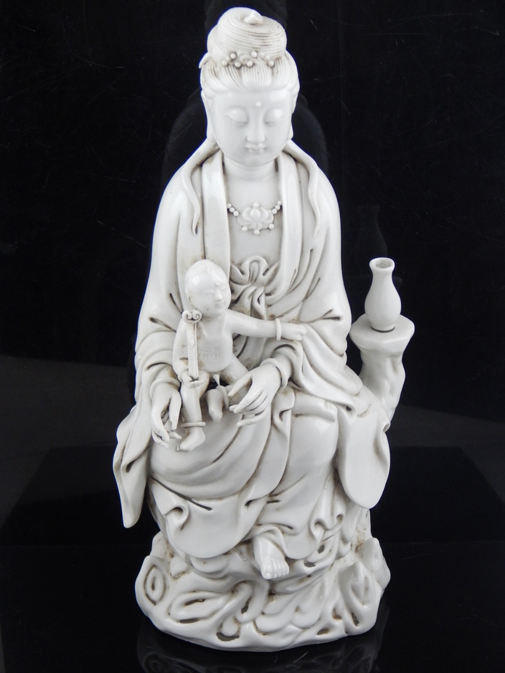 A Chinese blanc de chine figure of Guanyin holding a child, seated on a naturalistic base, bears