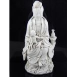 A Chinese blanc de chine figure of Guanyin holding a child, seated on a naturalistic base, bears