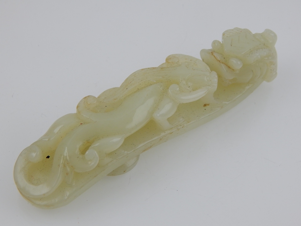A Chinese celadon jade belt buckle, carved as two dragons. L. 11cm