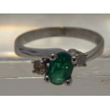 A white metal, diamond, and emerald crossover ring, the oval cut emerald of approx. 0.50 carats,