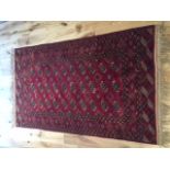 A red ground Bokhara rug, decorated with three rows of elephant pad medallions to centre,