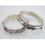 A pair of white metal bangles, decorated with stylised flowers. (2)